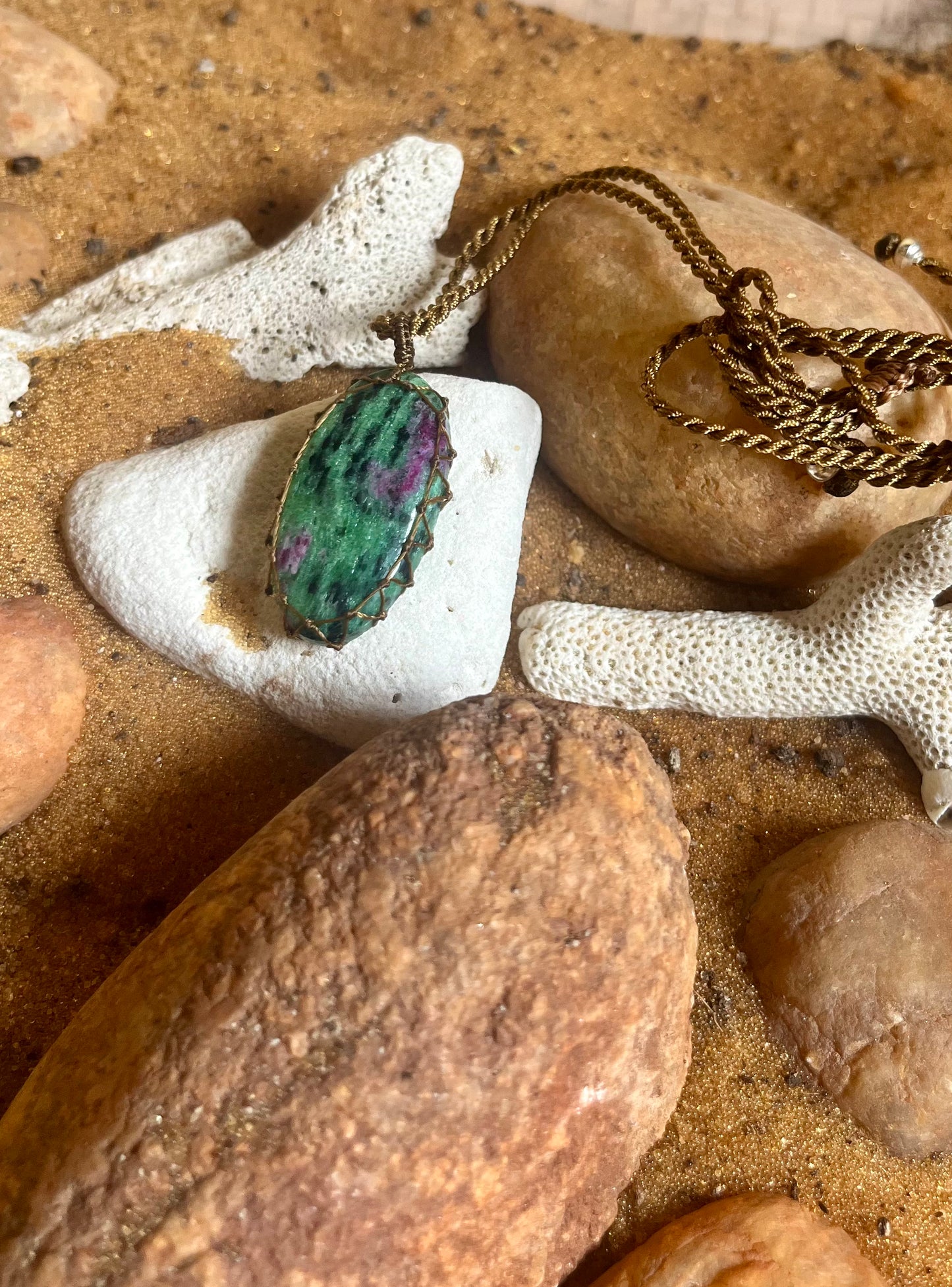Ruby Zoisite stone wrapped in natural macrame cord, showcasing the vibrant mixed red and green colors of this rare gemstone by Season Stones.