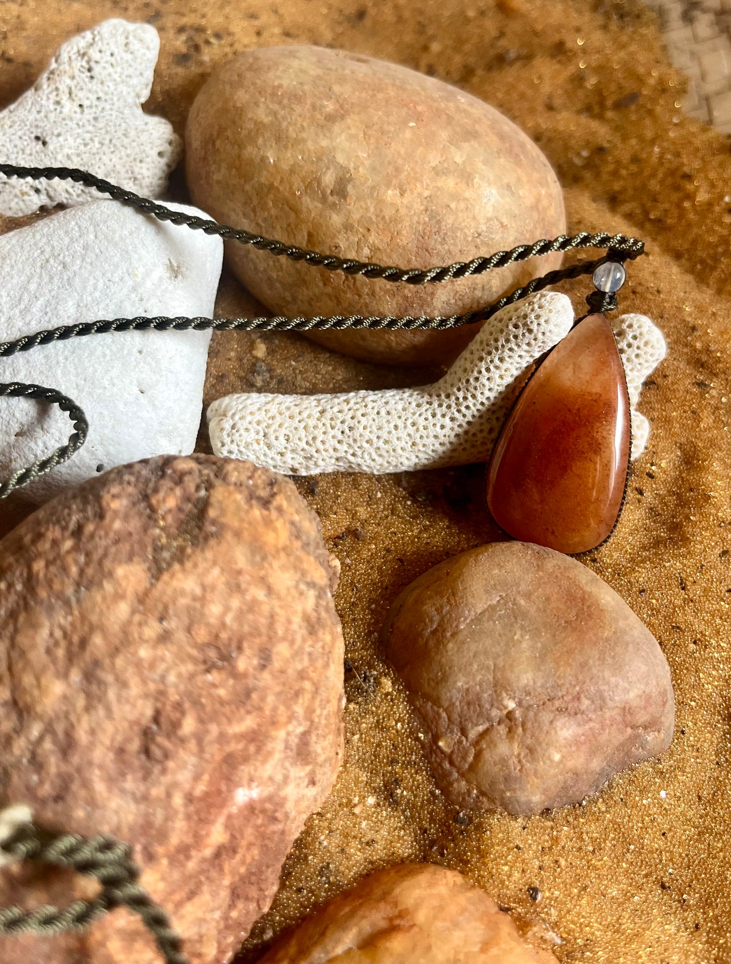 Carnelian pendant on macrame cord necklace by Season Stones, featuring a vibrant orange gemstone in a natural setting.