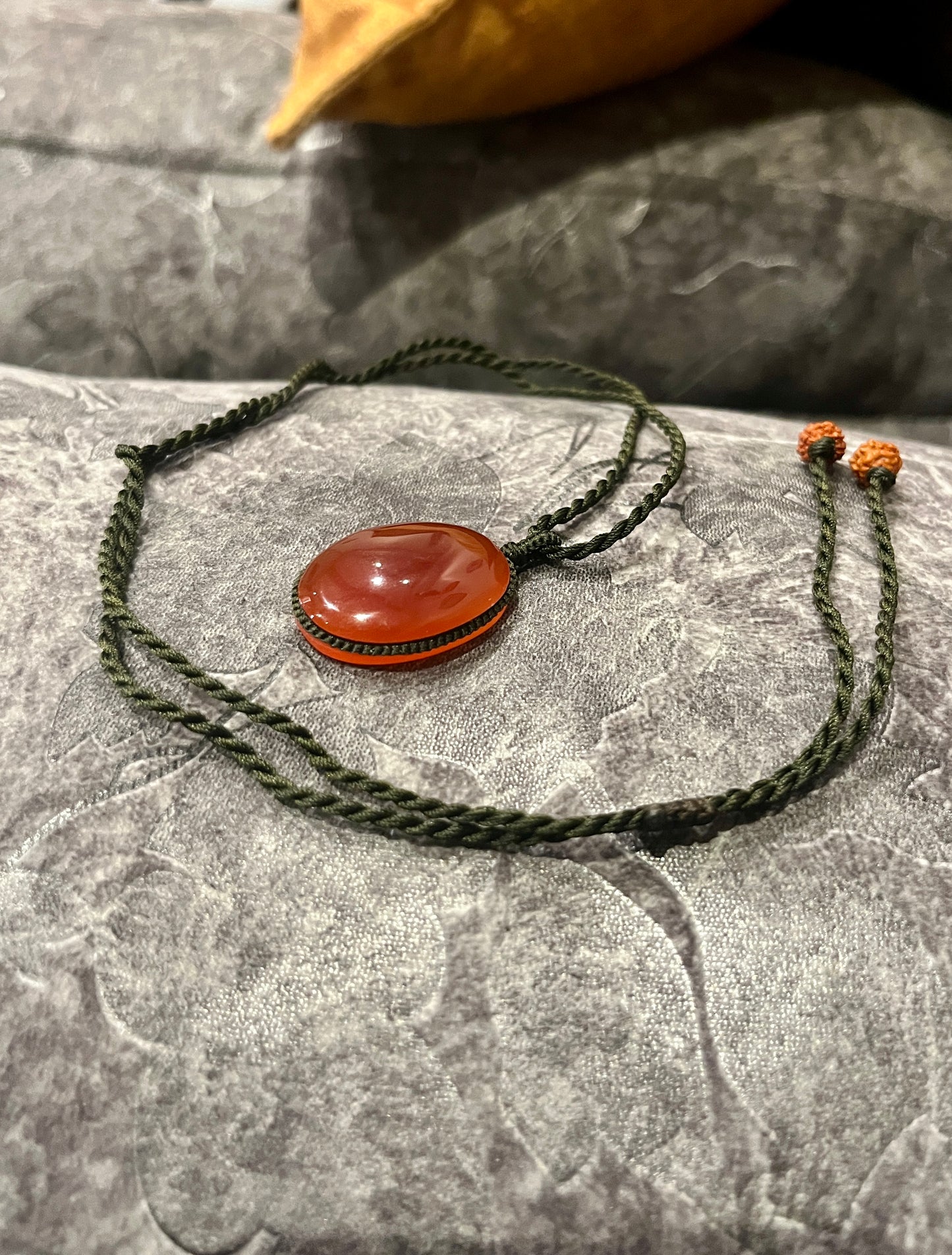 Carnelian pendant wrapped in macrame cord, featuring a vibrant orange gemstone on a seasonal stones chain, displayed against a neutral background.