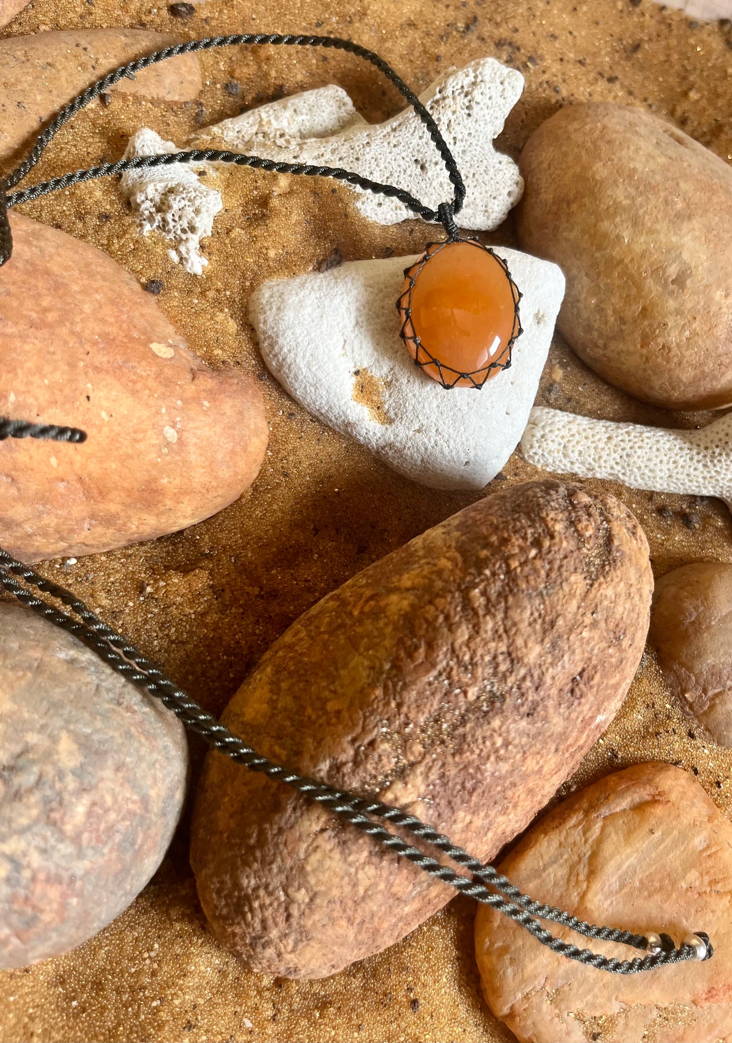 Carnelian stone pendant with woven macrame cord, handmade jewelry piece by Season Stones featuring vibrant orange gemstone.