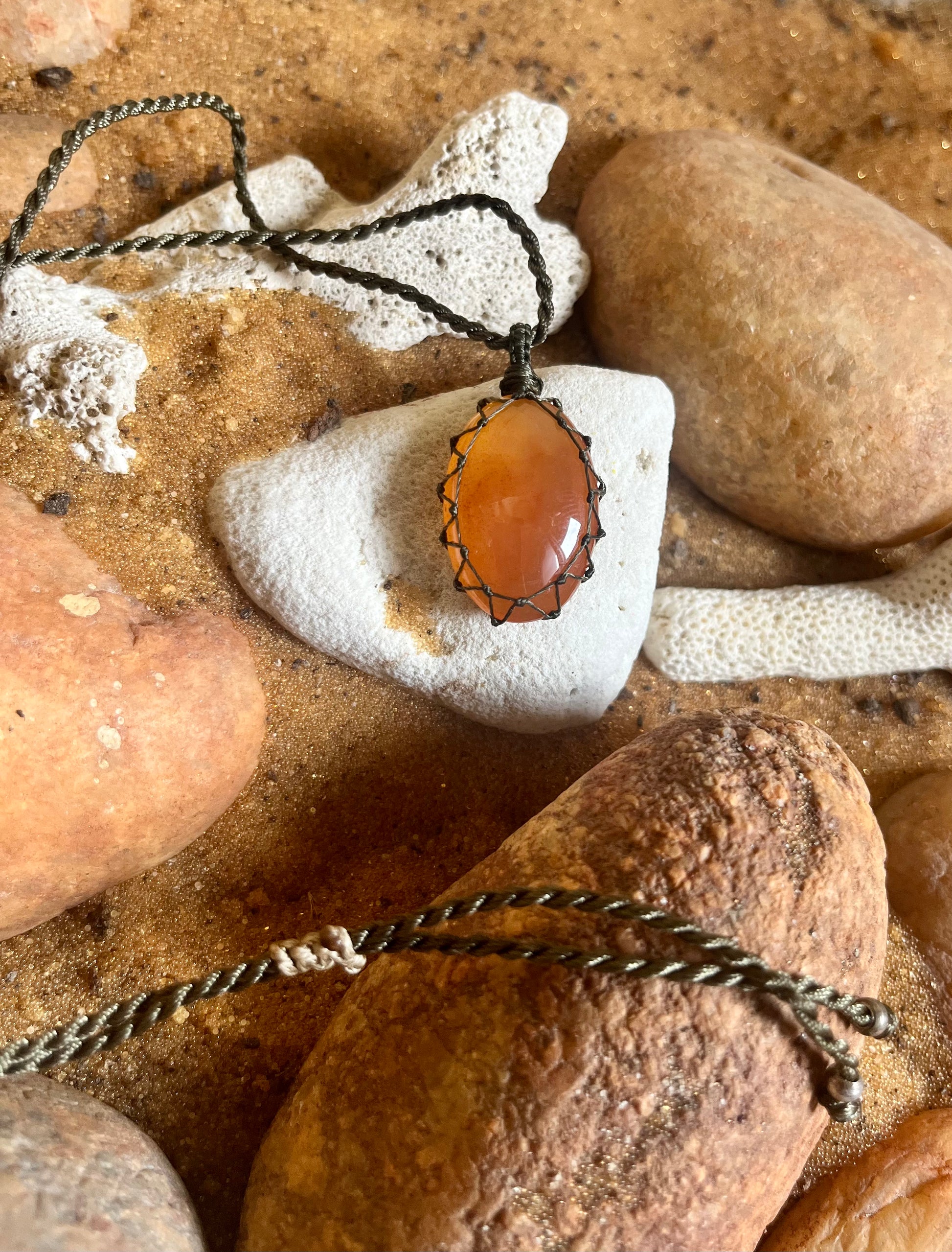 Carnelian pendant on macrame cord from Season Stones, featuring a polished orange gemstone with intricate knotting details.
